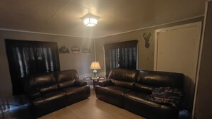 Een woonkamer met twee leren banken, een kleine tafel met een lamp en een aan de muur bevestigd decoratie van een hertenkop.