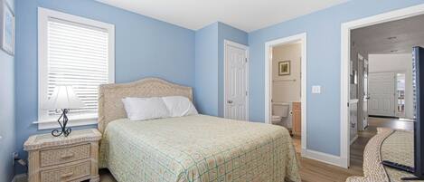 Un dormitorio con cama, mesita de noche, lámpara y una puerta que da al baño.
