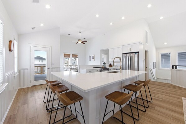 A spacious kitchen with a large island, wooden bar stools, stainless steel appliances, and a ceiling fan.