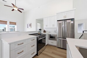 A modern kitchen with white cabinetry, stainless steel appliances, and a ceiling fan.