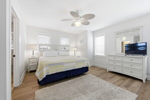 A bedroom with a bed, nightstands, a dresser, a television, a ceiling fan, and a window with blinds. - Sebastian by the Sea: Oceanside, Private Pool, Hot Tub, Foosball Table (Kill Devil Hills)
