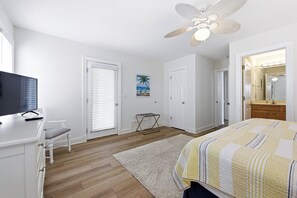 Un dormitorio con cama, escritorio, silla, ventilador de techo y baño con espejo.
