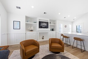 A modern kitchen with white cabinetry, a central island, and a flat-screen TV displaying 'Coastal Carolina Vacations and Sales'.