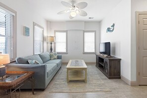 A living room with a sofa, a coffee table, a TV, a lamp, and a ceiling fan.
