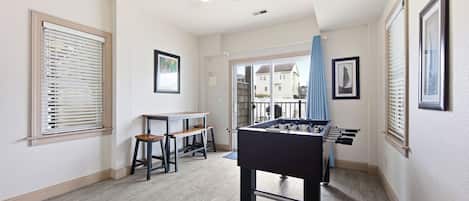 Una habitación con mesa de futbolín, una mesa con sillas y un ventilador de techo.