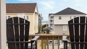 Vue depuis un balcon, avec deux fauteuils Adirondack, donnant sur un quartier résidentiel avec des maisons et une plage en arrière-plan.