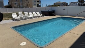 Una piscina rectangular con superficie azul cristalina, rodeada por una cerca blanca y sillas de descanso blancas alineadas a lo largo de la piscina.