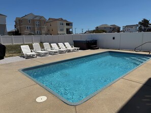 Una piscina rectangular con superficie azul cristalina, rodeada por una cerca blanca y sillas de descanso blancas alineadas a lo largo de la piscina.