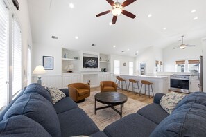 A spacious living room with a large sofa set, a coffee table, and a ceiling fan.