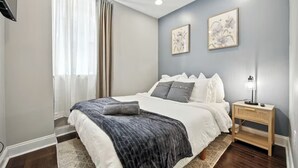A bedroom with a bed, a bedside table with a lamp, and two wall-mounted artworks. - Modern & Cozy 2-bedroom condo in Center City Philadelphia - Walk Everywhere (Philadelphia)
