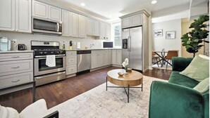 A modern kitchen with white cabinets, stainless steel appliances, and a dining area with a green sofa and a round coffee table. - Modern & Cozy 2-bedroom condo in Center City Philadelphia - Walk Everywhere (Philadelphia)