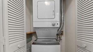 Une petite buanderie équipée d’un lave-linge à chargement frontal, d’un sèche-linge et d’un panneau de commande.