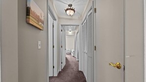 Un couloir avec des portes blanches, un sol recouvert de moquette et un luminaire au plafond.