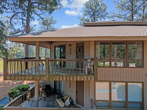 Une cabane à deux étages dotée d’une terrasse, de grandes fenêtres et offrant une vue sur la forêt environnante.