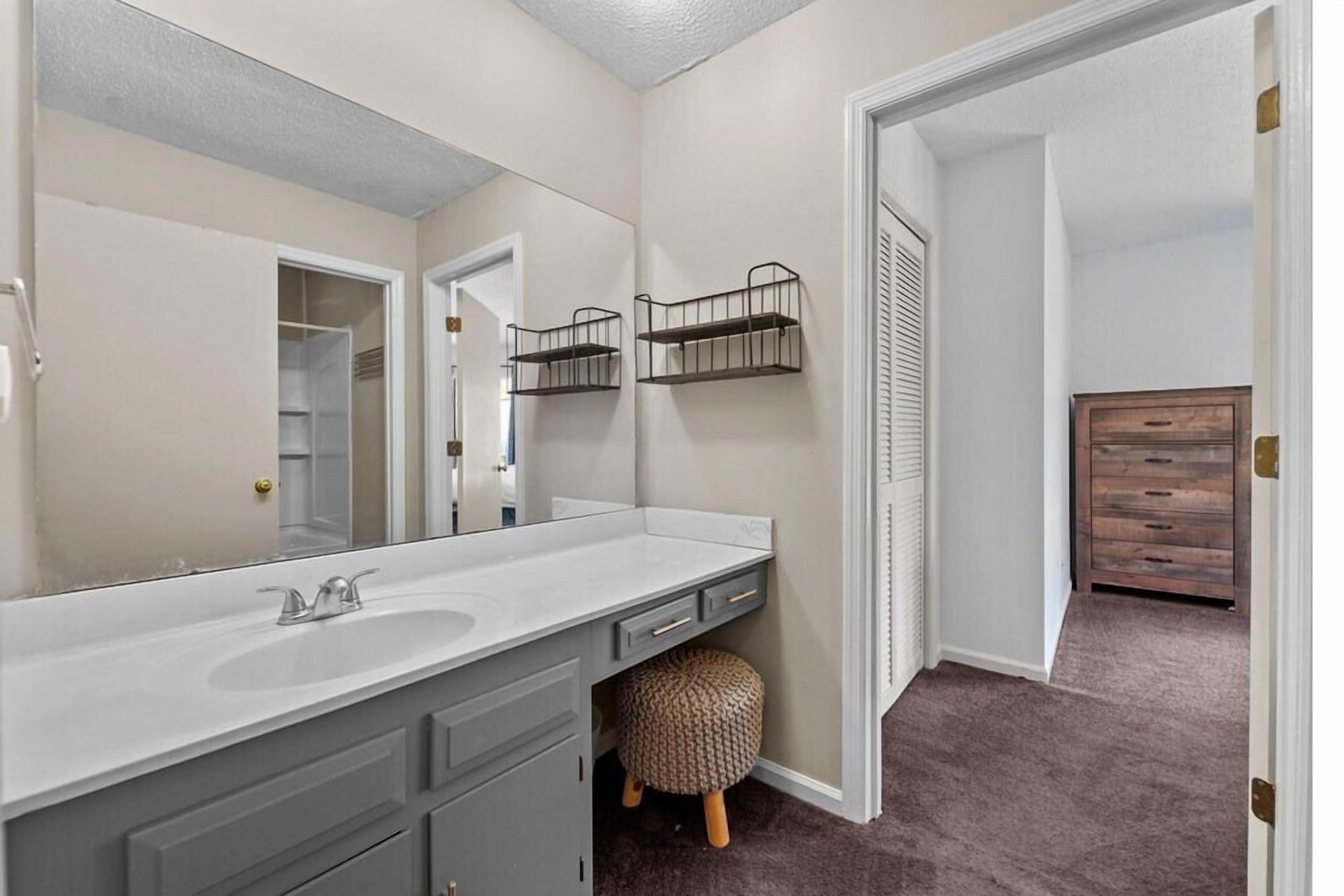 A bathroom with a white vanity, a large mirror, and a wooden stool.