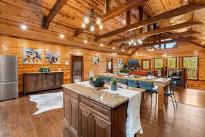 A spacious kitchen with a central island, wooden ceiling beams, and a large window overlooking a deck.