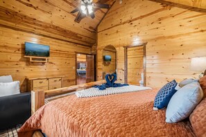 Une chambre dans une cabane en bois, avec un lit, des oreillers, une télévision et un ventilateur de plafond.