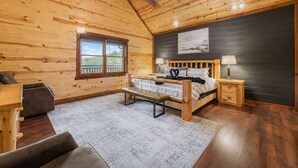 Een houten slaapkamer met een bed, een bankje, nachtkastjes en een raam met uitzicht.