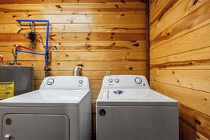 Une buanderie avec deux lave-linge et deux sèche-linge à chargement frontal, de couleur blanche, des murs en bois et des tuyaux apparents.