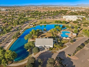 An aerial view of a residential area with multiple swimming pools, a large building, and surrounding greenery.