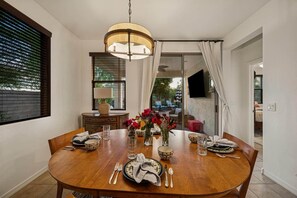 A dining area with a round wooden table set for four, a hanging light fixture, and a view of the outdoors through a sliding glass door. - Heated Pool Oasis | Family Retreat in Gilbert (Gilbert)