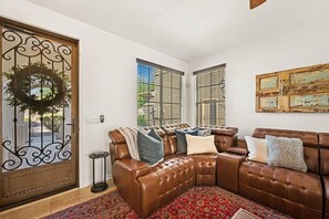 A living room with a brown leather sectional sofa, a patterned rug, and a decorative wreath on the door. - Heated Pool Oasis | Family Retreat in Gilbert (Gilbert)