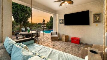 Une terrasse ensoleillée avec une piscine, du mobilier d’extérieur et un ventilateur de plafond.