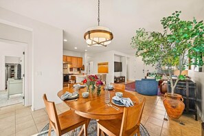 A dining area with a wooden table set for four, a hanging light fixture, and a potted plant. - Heated Pool Oasis | Family Retreat in Gilbert (Gilbert)