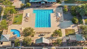Una vista aerea di un resort con una grande piscina centrale, diverse zone relax e varie disposizioni di sedute all'aperto.