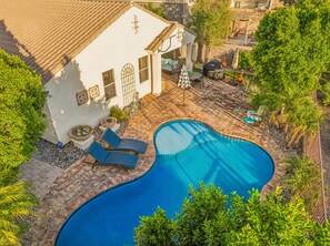 A swimming pool with lounge chairs, a covered patio, and a white building with a cross on the roof. - Casa de Stella Luna • European Cottage with HEATED Pool in Power Ranch (Gilbert)