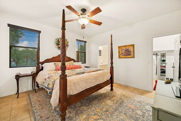 A four-poster bed with a ceiling fan, a patterned rug, and a wooden nightstand.