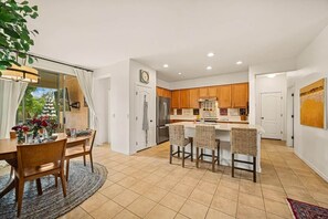A modern kitchen with wooden cabinets, a refrigerator, and a dining area with a table and chairs. - Heated Pool Oasis | Family Retreat in Gilbert (Gilbert)