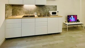 Cocina moderna con armarios blancos, microondas, fregadero y televisor sobre una mesita.