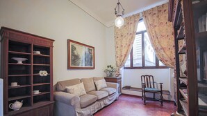 A cozy living room with a sofa, a wooden cabinet with shelves, a chair, and a window with curtains.