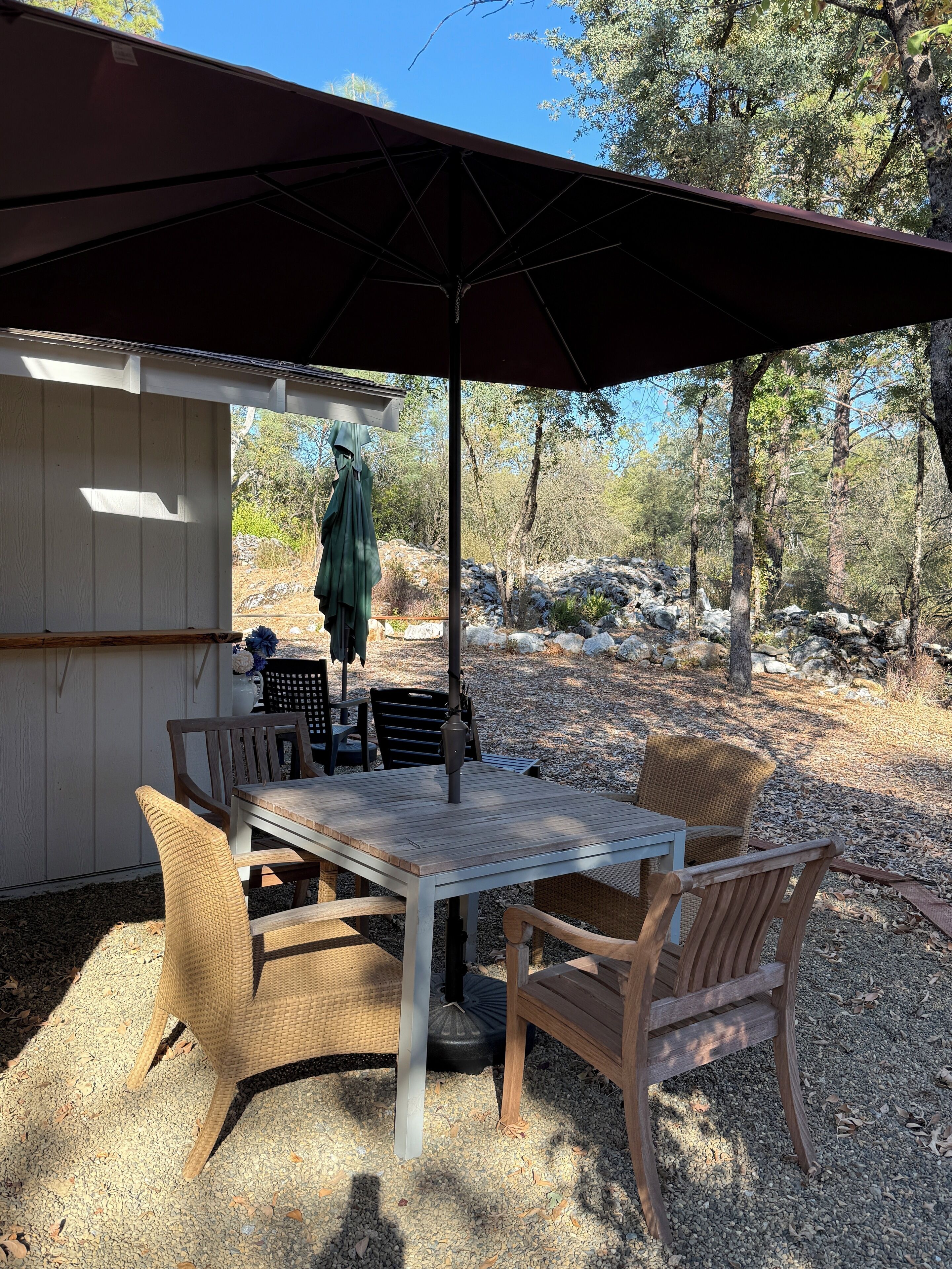 Une terrasse extérieure avec une table et des chaises, un parasol et une vue sur une zone boisée.