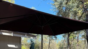 Un patio al aire libre con una mesa y sillas, una sombrilla y vistas a un área boscosa.