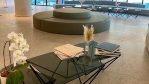 A modern lobby with a glass coffee table, seating area, and large windows offering a view of the outdoors. - PORTO ALTO RESORT - MARÉ ALTA (Ipojuca)