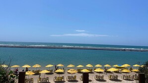 A beach with yellow umbrellas and chairs, a clear sky, and the ocean in the background. - PORTO ALTO RESORT - MARÉ ALTA (Ipojuca)