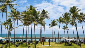 A beachside resort with palm trees, outdoor seating, and a view of the ocean. - PORTO ALTO RESORT - MARÉ ALTA (Ipojuca)
