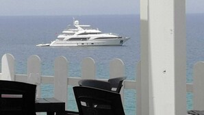 Blick auf eine große Yacht auf dem Wasser vom Balkon mit weißen Geländern und einem Tisch mit Stühlen.