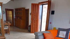 Ein Wohnzimmer mit grauem Sofa, orangefarbenen Kissen und einem Holzessttisch mit Stühlen.