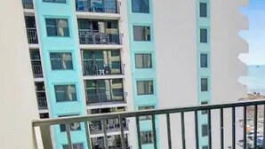 Parveke, jossa on turkoosinsiniset tuolit, näkymä monikerroksiseen rakennukseen, jossa on myös parvekkeita, ja kirkas taivas.