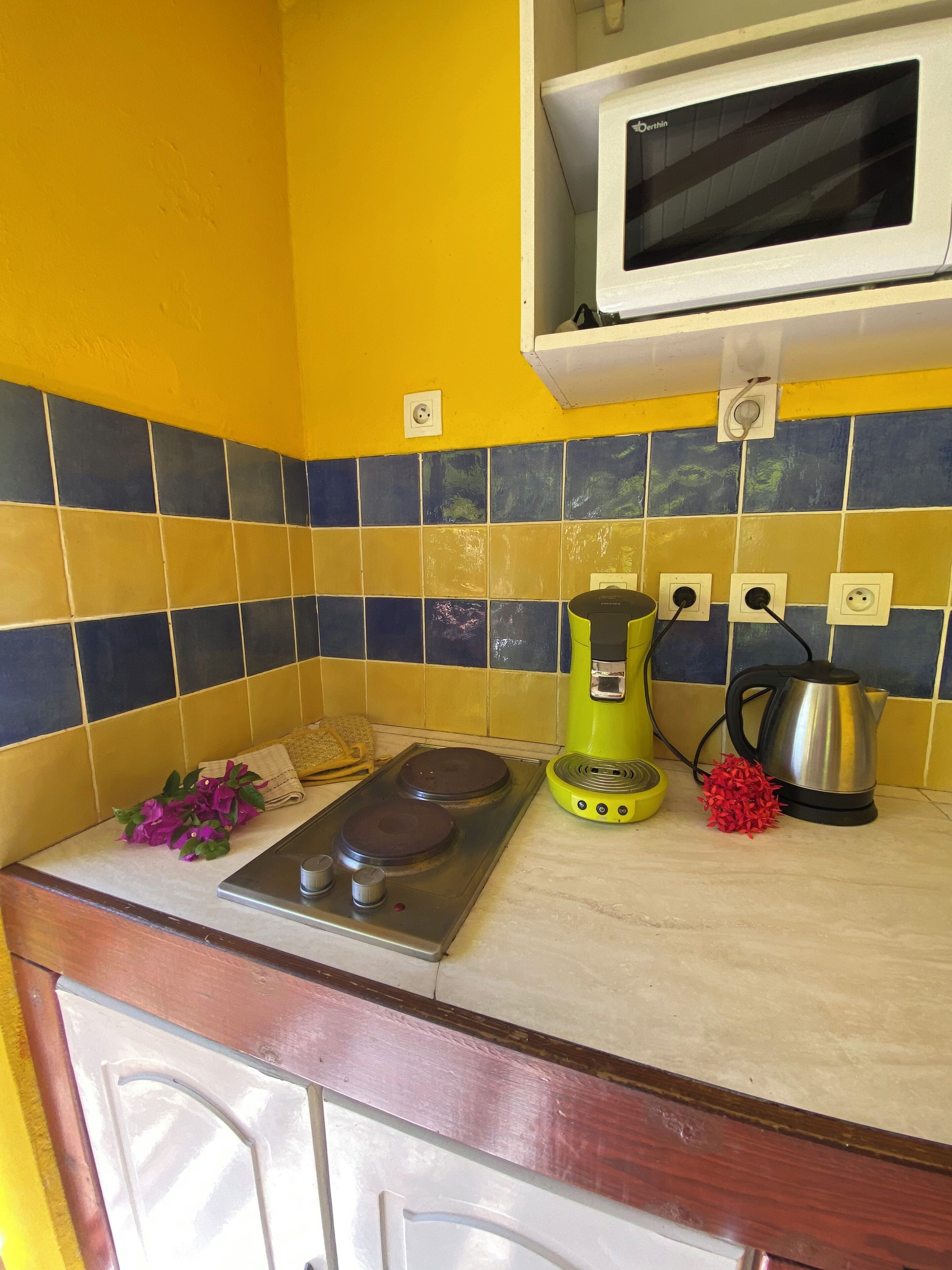 A kitchen with yellow walls, a stove, a green electric kettle, a silver kettle, and a microwave.