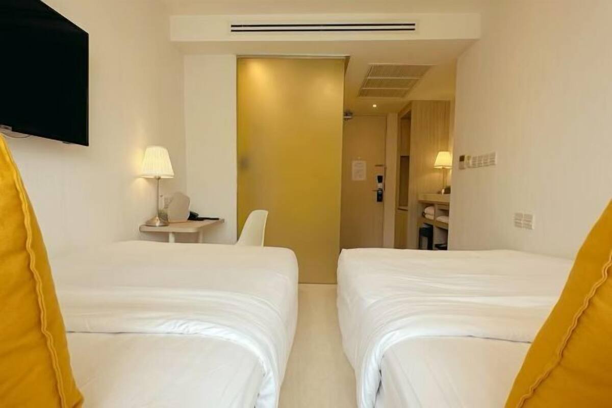 Ein Hotelzimmer mit zwei Betten, einem Schreibtisch mit Lampe, einem Fernseher und einem durch eine offene Tür einsehbaren Badezimmer.
