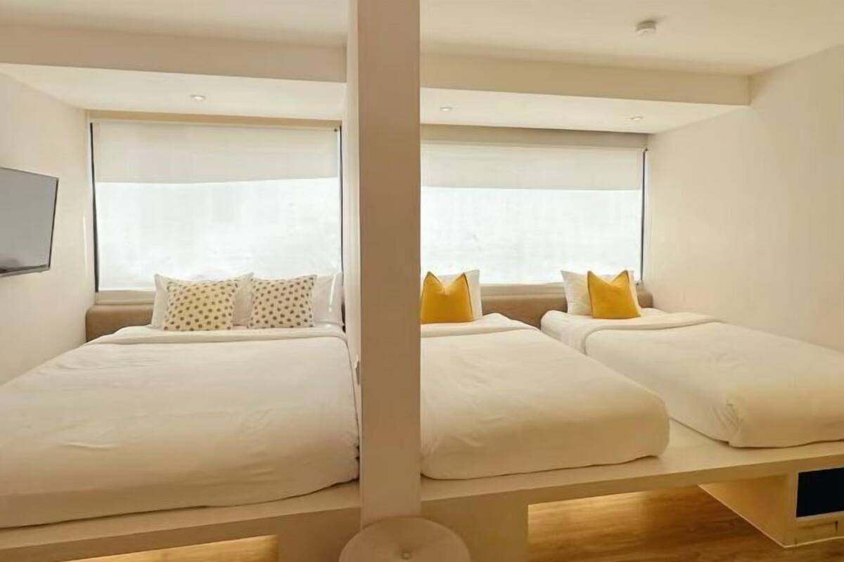 Ein Schlafzimmer mit zwei Betten, jeweils mit weißer Bettwäsche und Kissen, sowie einem an der Wand montierten Fernseher.