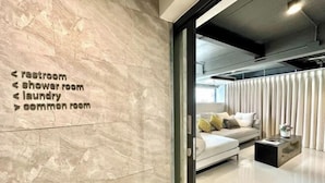 Een moderne hotelkamer met een marmeren wand en bewegwijzering naar faciliteiten zoals het toilet, de doucelocatie, wasserette en gemeenschappelijke ruimte.