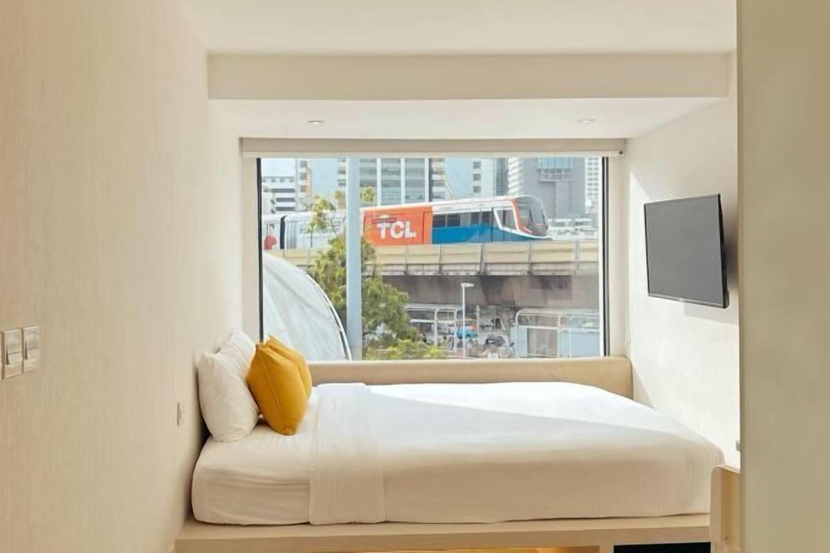 Ein modernes Hotelzimmer mit Bett, Fenster mit Stadtblick und einem an der Wand befestigten Flachbildfernseher.