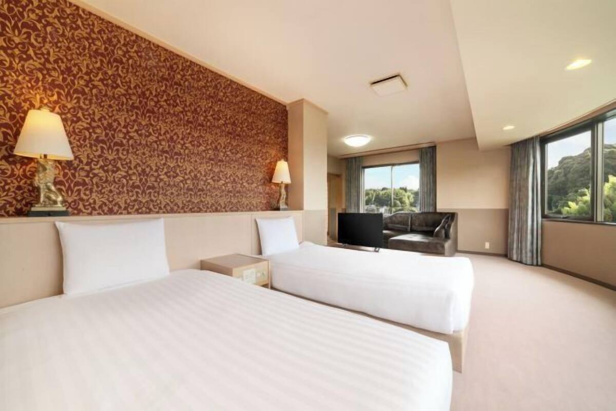 Habitación de hotel con dos camas, televisión, sofá y un ventanal con vistas.