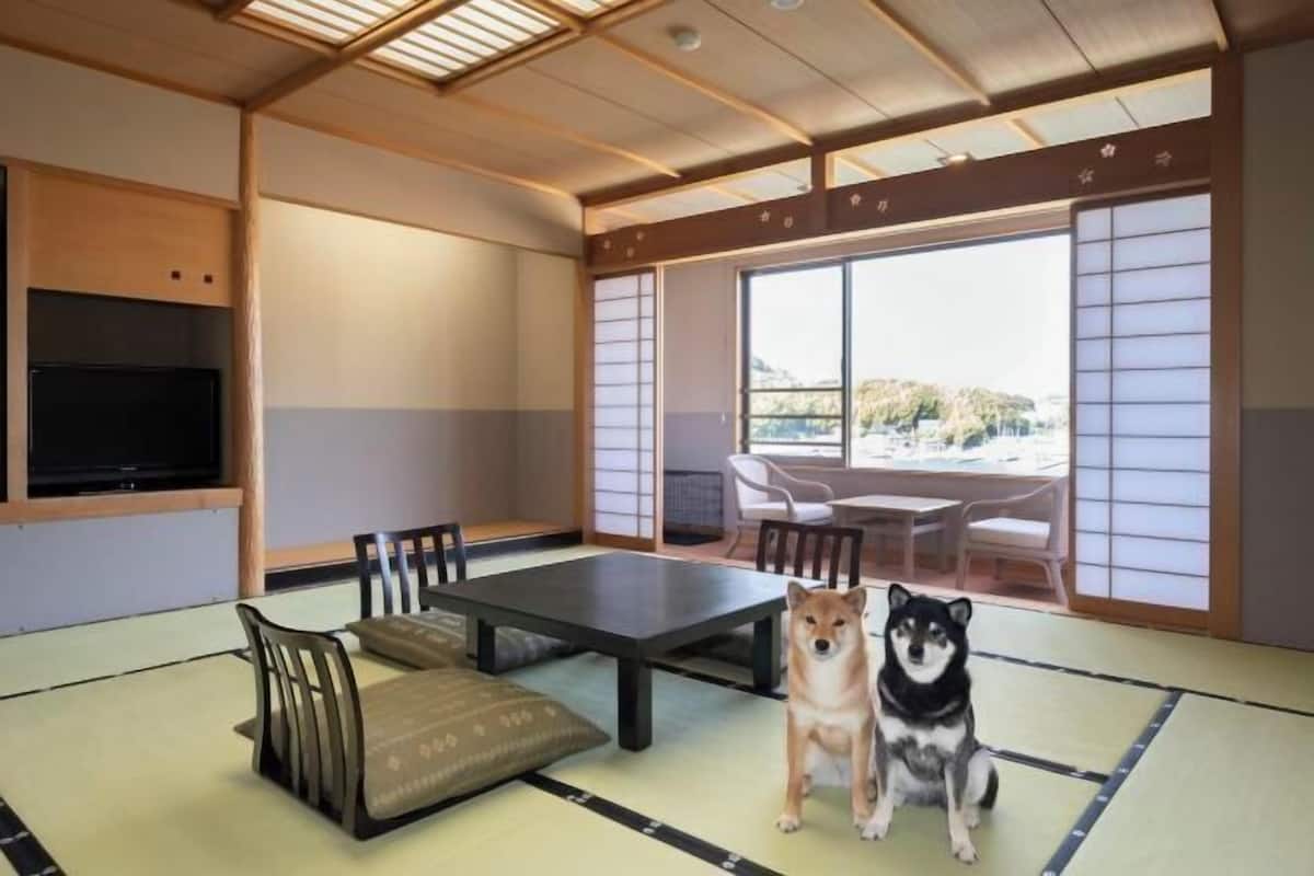 Una habitación japonesa tradicional con suelo de tatami, una mesa baja, sillas, un televisor y un perro.