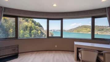 Ein Zimmer mit gewölbter Decke, großen Fenstern mit Blick auf eine Küstenlandschaft, einem Schreibtisch mit Stühlen und einem kleinen, abgegrenzten Bereich mit einem Metallgitter.